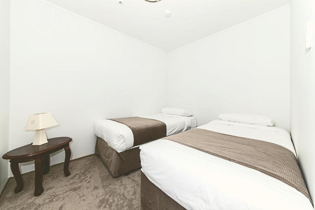 a room with two beds and a table with a lamp at Airport Gateway Hotel in Auckland