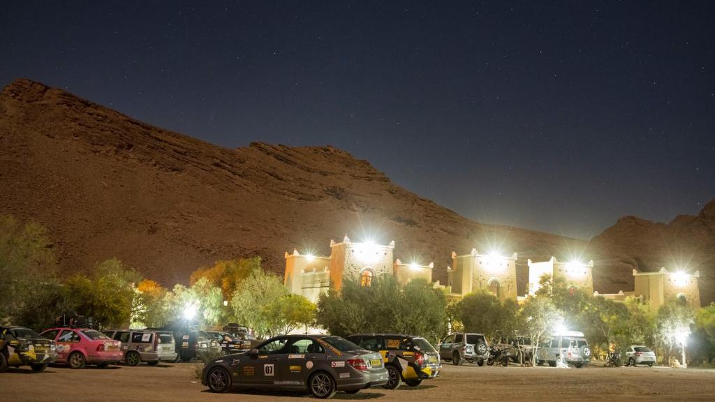 a group of cars parked in a parking lot in front of a mountain at Kasbah Hotel Camping Jurassique in Ifri