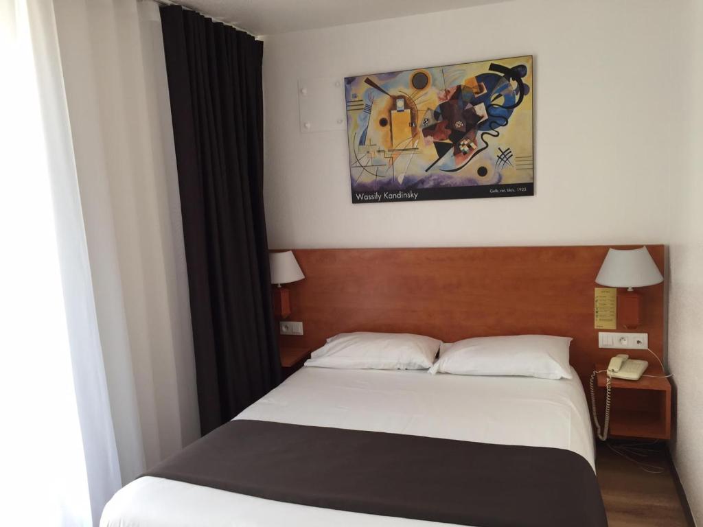 a bedroom with a bed, a desk, and a painting on the wall at Hotel Le 21ème in Strasbourg