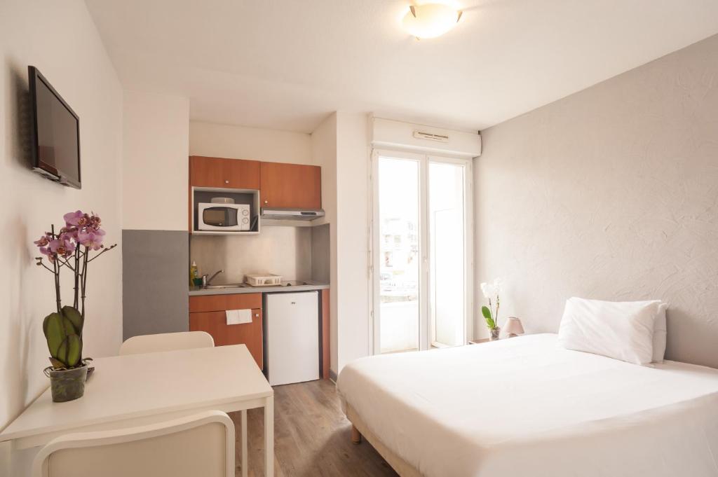 a small room with a white bed and a kitchen at City Résidence Chelles in Chelles