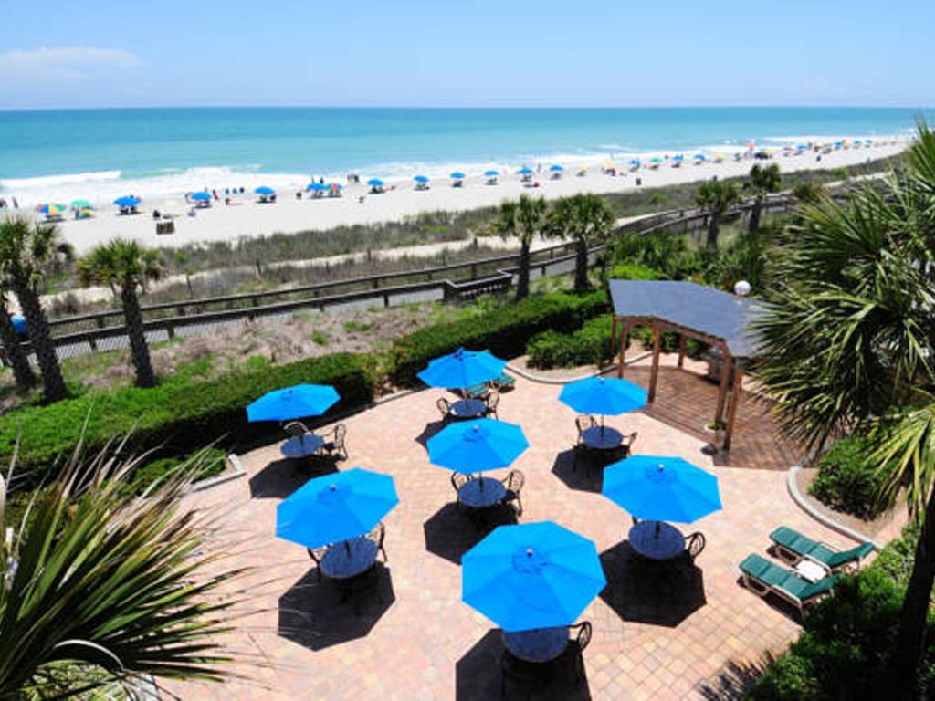 a patio with blue umbrellas and the beach at Holiday Pavilion Resort on the Boardwalk in Myrtle Beach