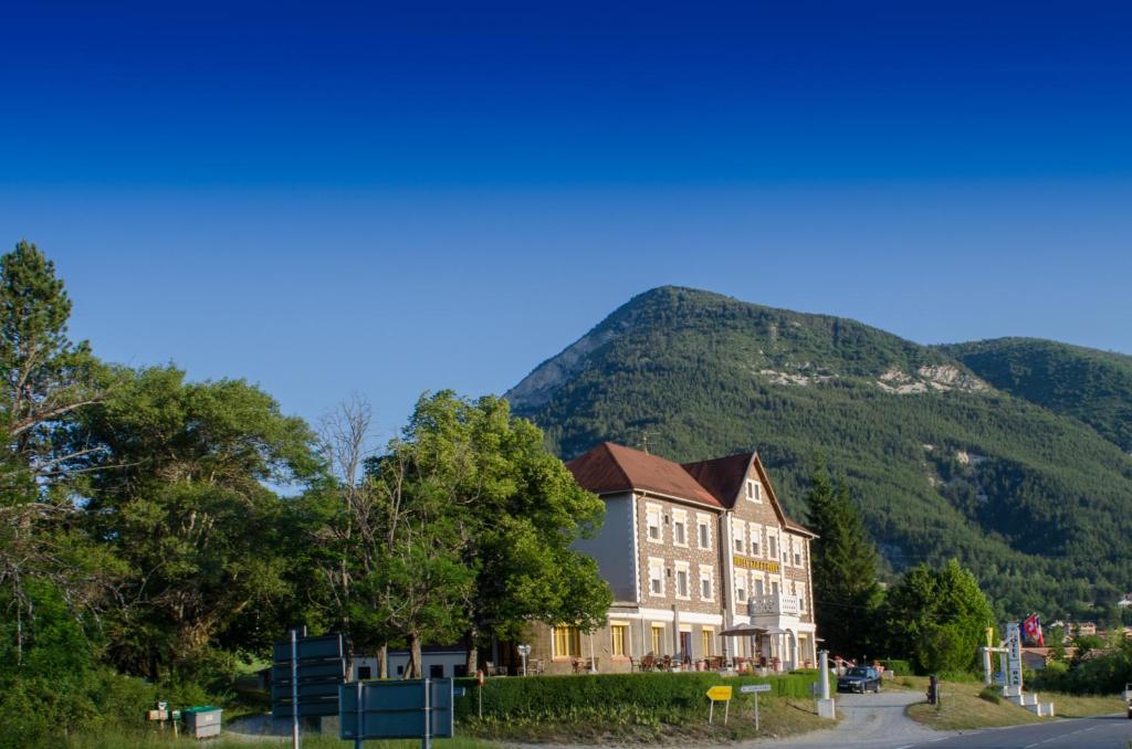 a large building with a mountain in the background at Hôtel Lac Et Forêt in Saint-André-les-Alpes