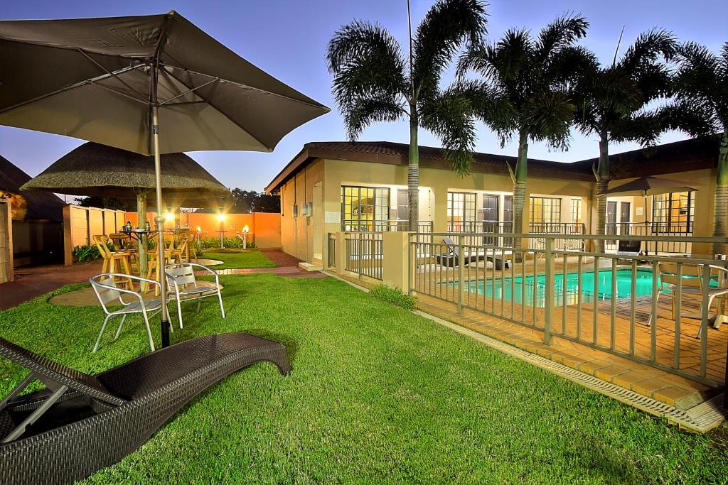 a house with a yard with chairs and an umbrella at Gecko Inn in Richards Bay