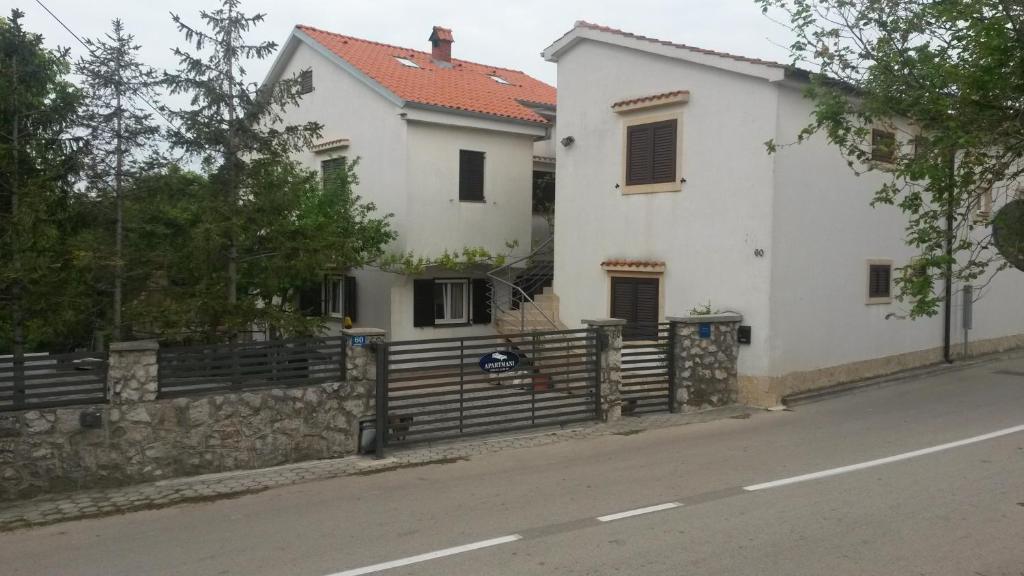 een wit huis met een hek naast een straat bij Apartmani Božić-Omišalj in Omišalj