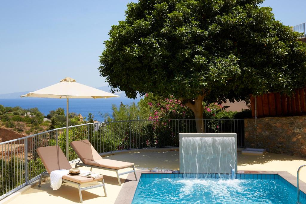 een zwembad met 2 stoelen en een parasol bij Pleiades Luxurious Villas in Agios Nikolaos