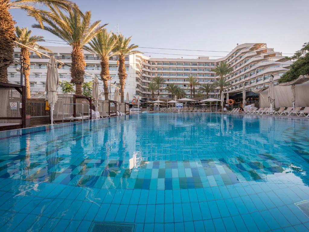 a large swimming pool with a hotel in the background at Neptune Eilat By Dan Hotels in Eilat