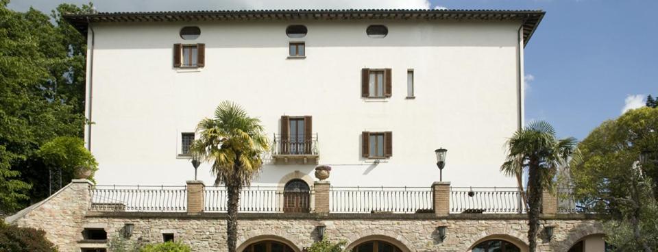 un gran edificio blanco con palmeras delante en Hotel Fontemaggio en Assisi