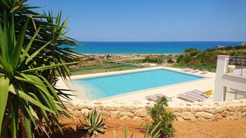 a swimming pool with chairs and the ocean in the background at La Blanca Resort & Spa in Castellammare del Golfo