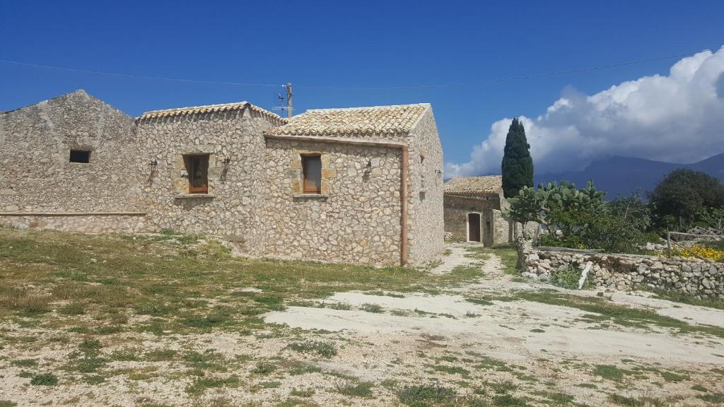 un vecchio edificio in pietra con un campo di fronte di Vecchio Baglio Cofano a Custonaci