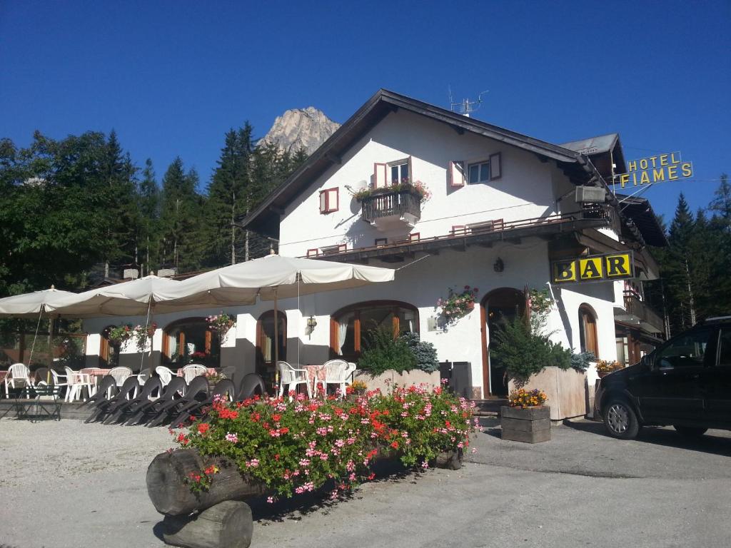 a white building with tables and chairs and flowers at Hotel Fiames in Cortina dʼAmpezzo