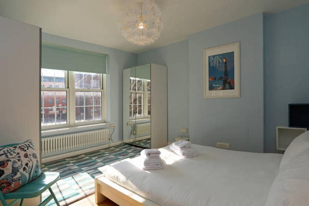 a bedroom with a bed and a chair and two windows at Riverside Cutty Sark 2BD Retreat in London