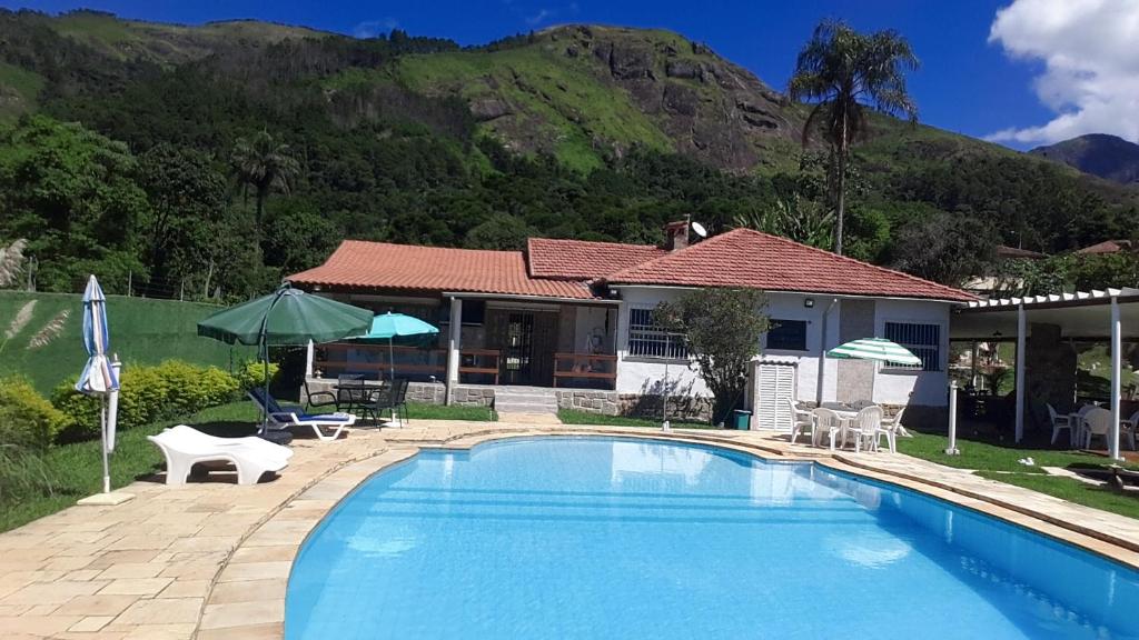 a swimming pool in front of a house with a mountain at Sítio Corta Vento in Teresópolis