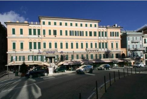 een groot gebouw met auto's geparkeerd voor een straat bij Hotel Mediterranee in Genua