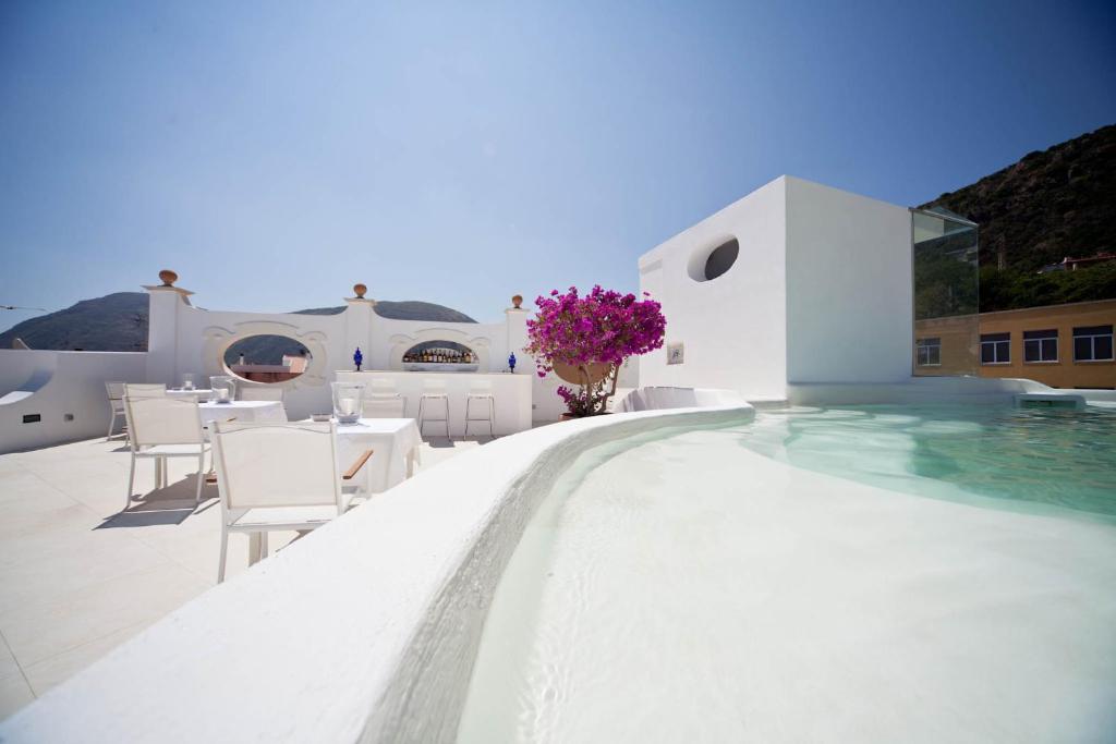 una piscina con mesas blancas, sillas y flores en un edificio en La Settima Luna Hotel en Canneto