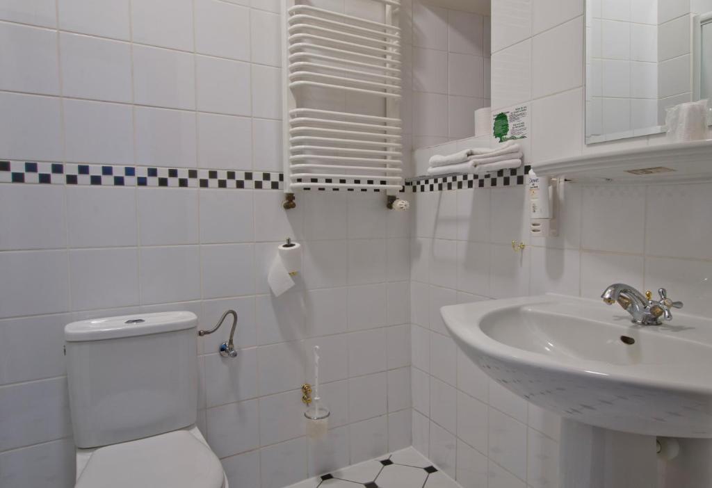 White tiled bathroom with sink, toilet, towel rack, and checkered border.