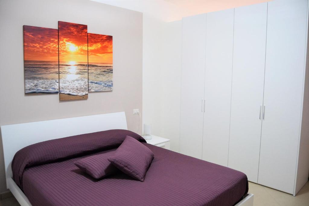 マリーナ・ディ・カメロータにあるCosta del Soleのベッドルーム1室(壁に3つの絵画が飾られた紫色のベッド1台付)