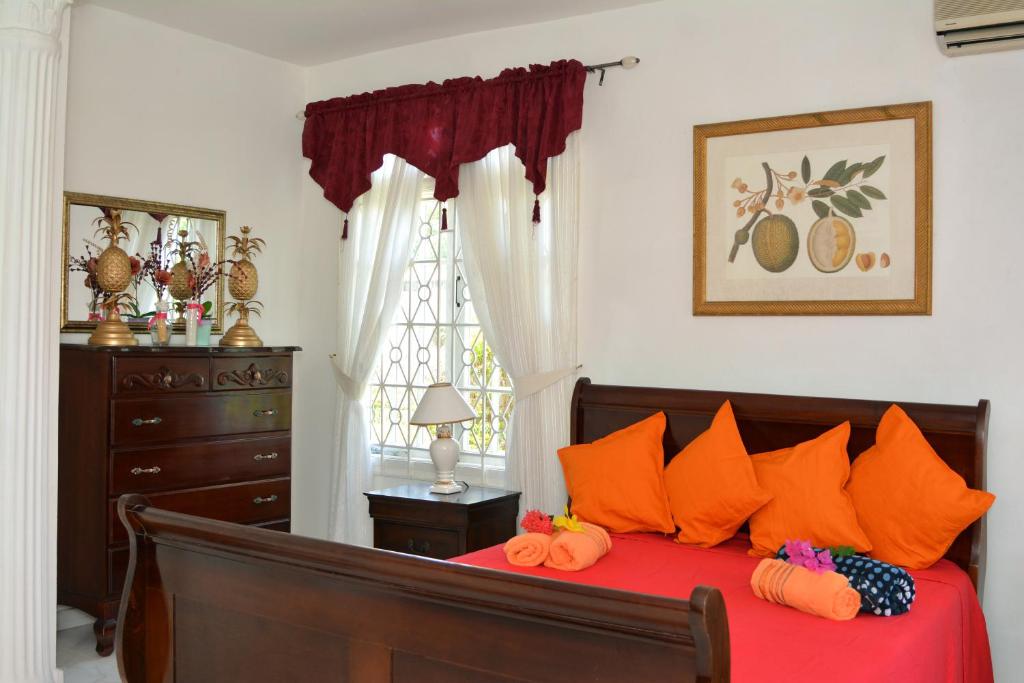 a bedroom with a bed with orange pillows and a dresser at Paradise Palms Jamaica Vacation Rental in Montego Bay