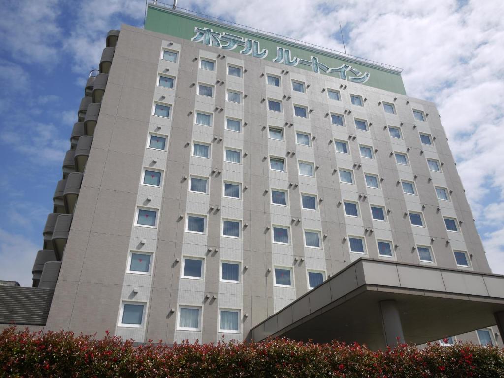 Ein hohes weißes Gebäude mit einem Schild drauf. in der Unterkunft Hotel Route-Inn Iwakiizumi Ekimae in Iwaki