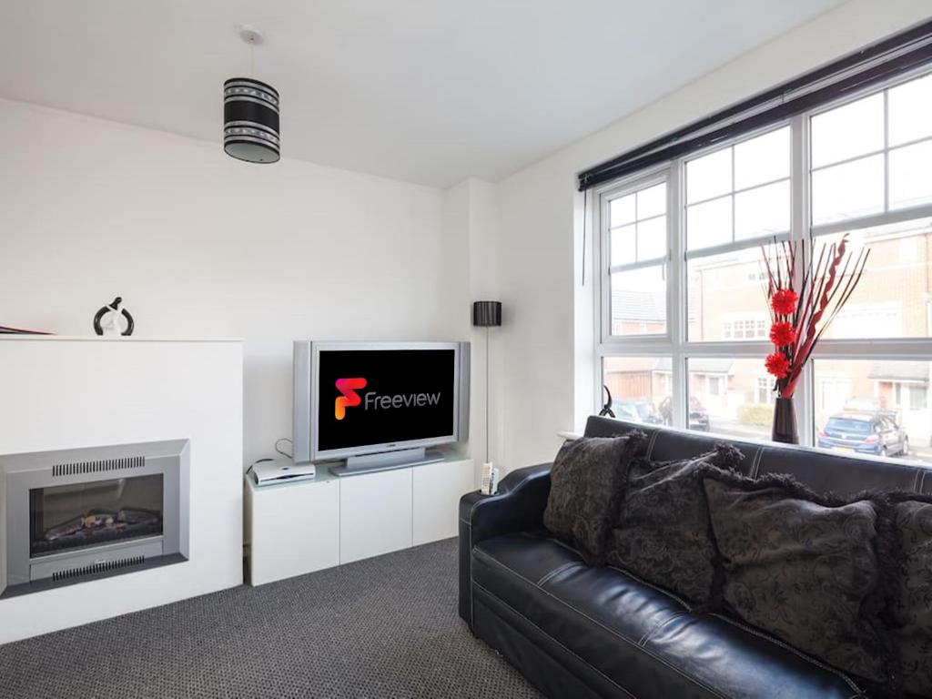 a living room with a black leather couch and a television at My-Places Abbotsfield Court Townhouse in Manchester