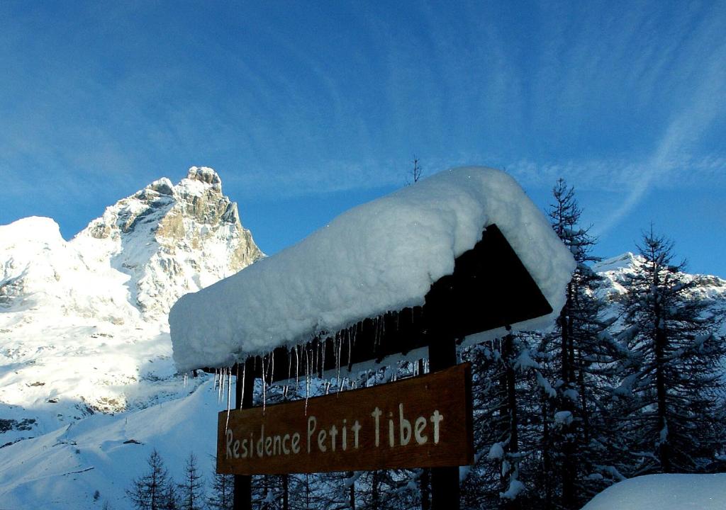 a snow covered sign in front of a mountain at Residence Petit Tibet in Breuil-Cervinia