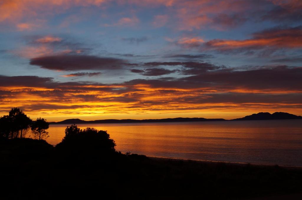 a sunset on a beach with the water and mountains at Swansea Beach House Oceanfront in Swansea