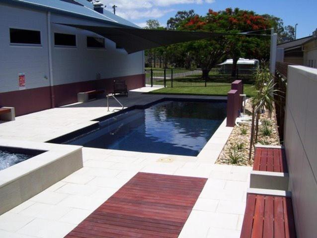 a swimming pool in front of a house with a red bench at Fraser Coast Top Tourist Park in Hervey Bay