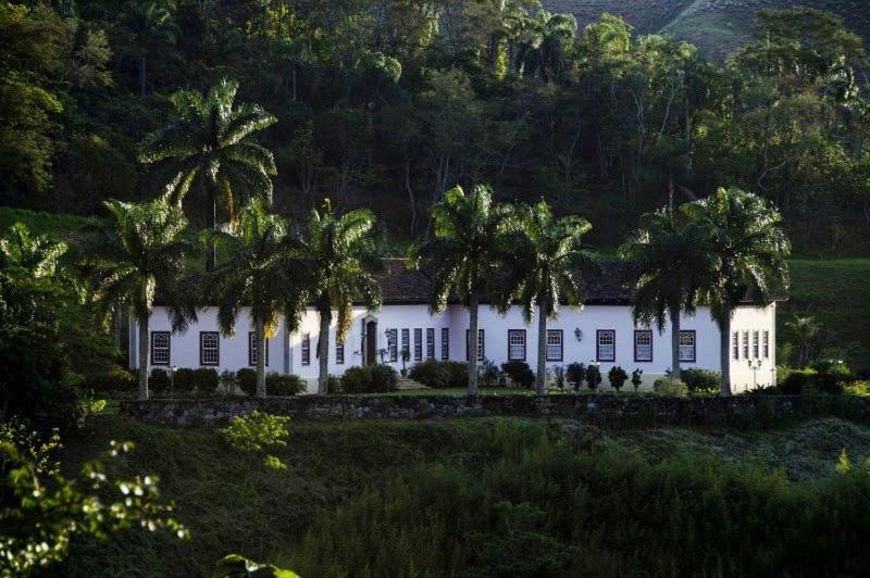 a white house with palm trees in a field at Fazenda Cachoeira Grande in Vassouras