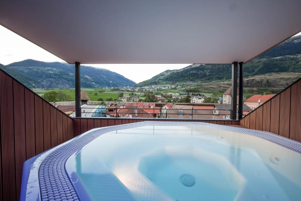 a hot tub on a balcony with mountains in the background at Hotel Gasthof Grüner Baum in Glorenza