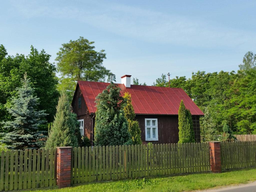 a house with a red roof behind a fence at Domek Drewniany in Nowa Wola