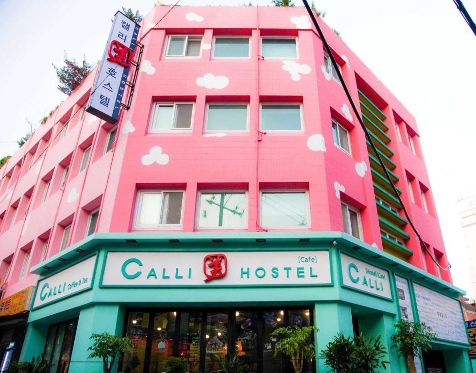 釜山的住宿－卡利旅館，街上的粉红色建筑,有商店