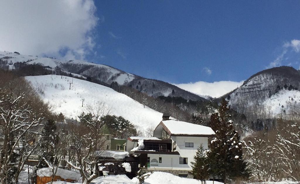 a house in the snow next to a mountain at Hakuba Landmark Happo Lodge in Hakuba