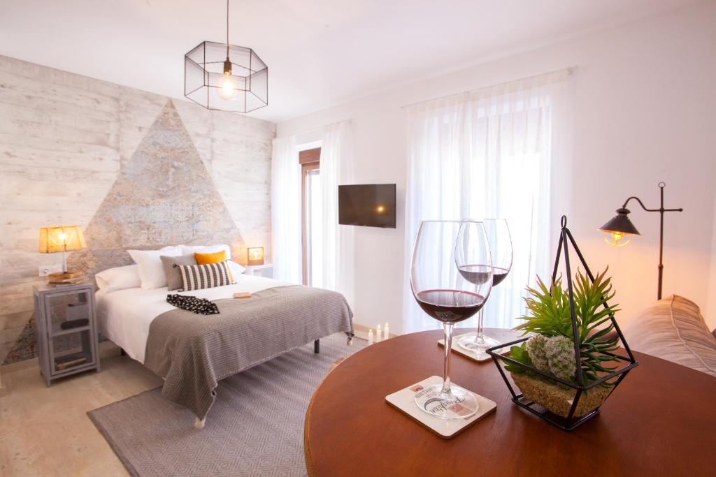 Lukanda Mariana في إشبيلية: غرفة نوم مع سرير وطاولة مع كؤوس للنبيذ