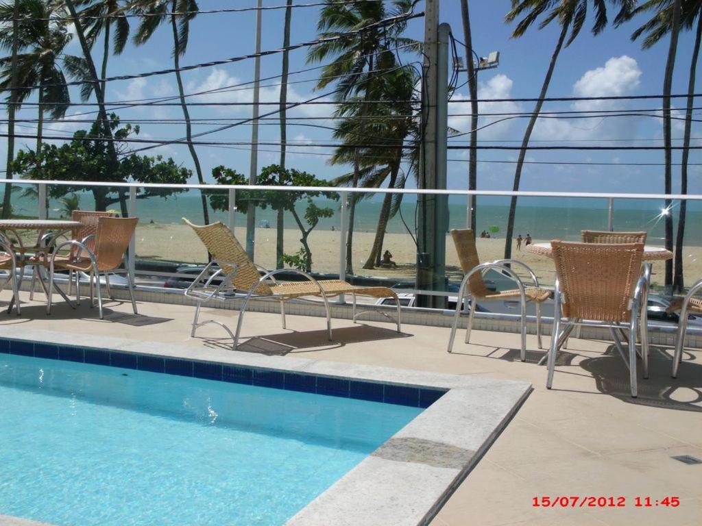 una piscina con sillas y una mesa y la playa en Apartamento Orla do Cabo Branco, en João Pessoa