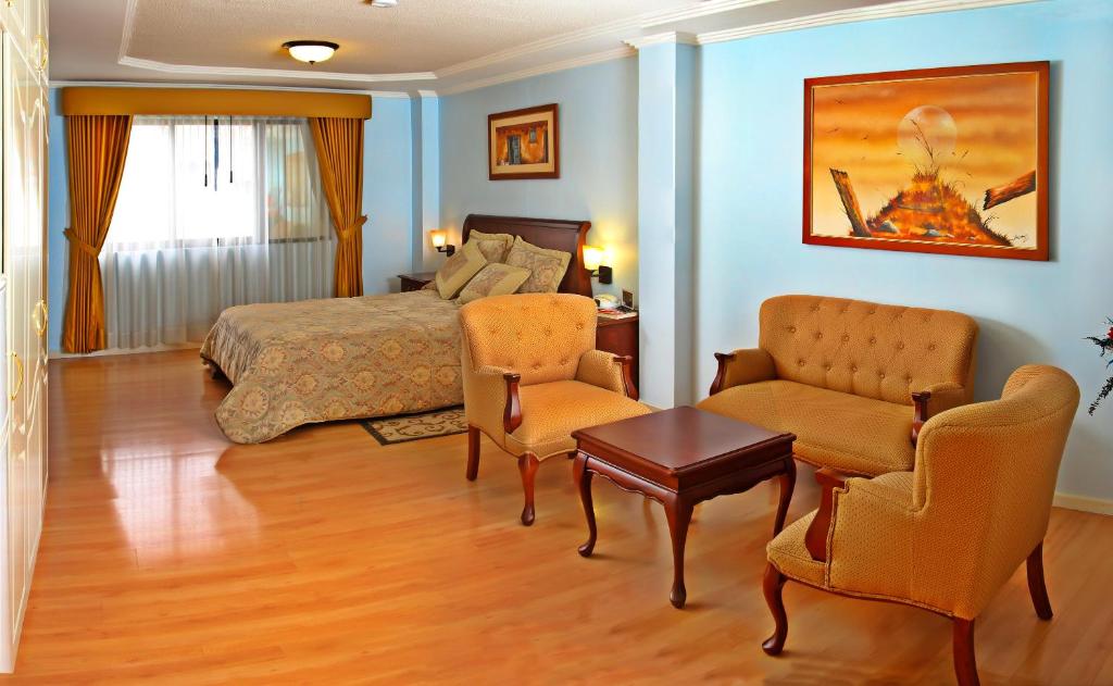 a bedroom with a bed and two chairs and a table at Hotel Yanuncay in Cuenca