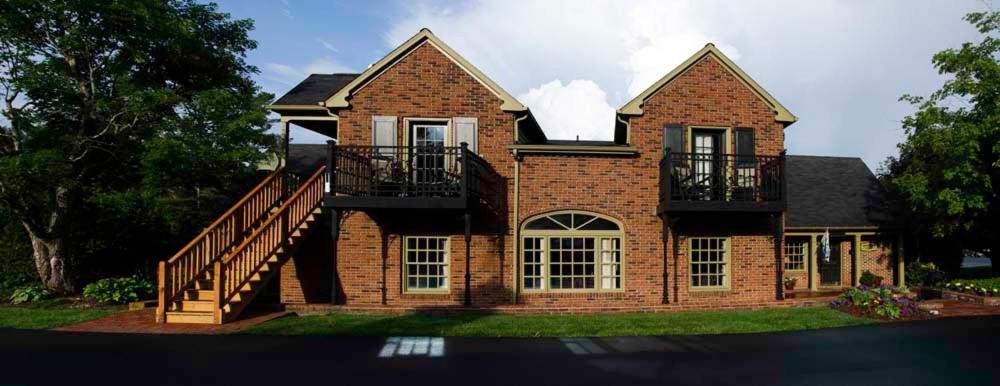 The Hillwinds Inn in Blowing Rock, NC, showcasing a brick building with two stories, wooden staircases, balconies, and a landscaped lawn under a partly cloudy sky.