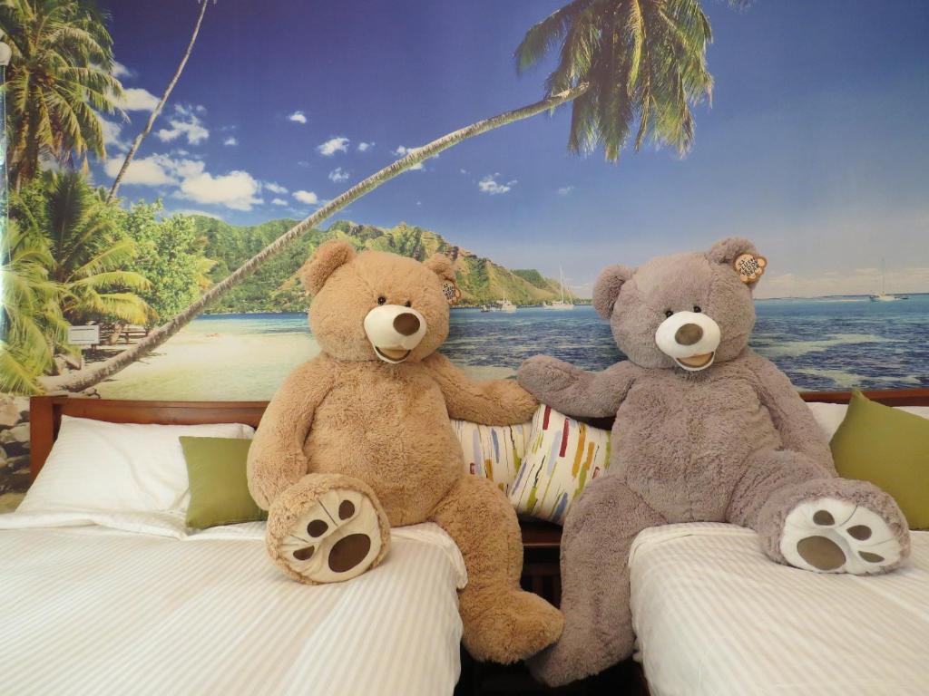 two teddy bears sitting on beds in front of a mural at Hai Yang Homestay in Ji'an