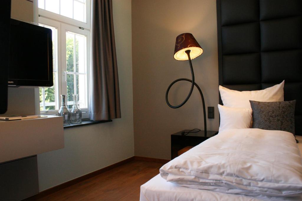 a bedroom with a bed with a lamp and a television at Hotel Rosenmeer in Mönchengladbach