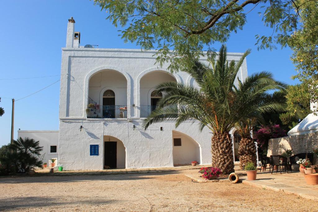a white building with a palm tree in front of it at Masseria Gianecchia in Cisternino