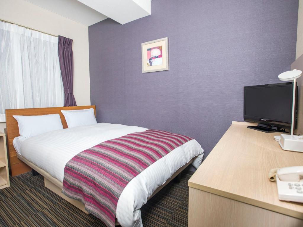 a hotel room with a bed and a desk with a television at FLEXSTAY INN Shinagawa in Tokyo