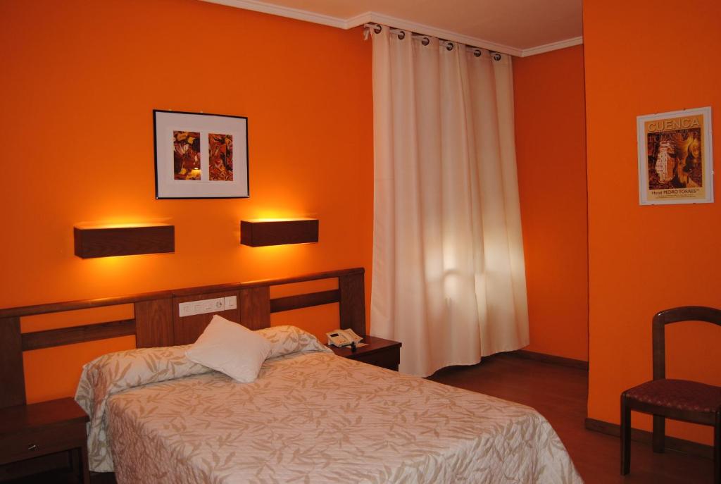 Schlafzimmer mit orangefarbenen Wänden, einem Bett und einem Stuhl in der Unterkunft Hotel Pedro Torres in Cuenca