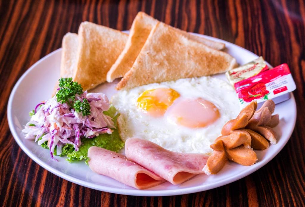 A fried-egg breakfast plate with ham, sausage, toast and salad.