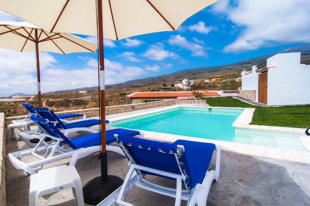 a villa with a swimming pool with chairs and an umbrella at Casa Rural La Pardela in La Cisnera