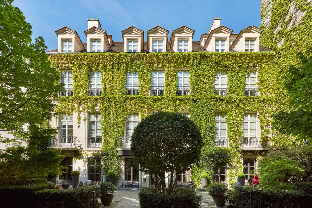 un bâtiment recouvert de lierre avec un arbre en face dans l'établissement Le Pavillon de la Reine & Spa, à Paris