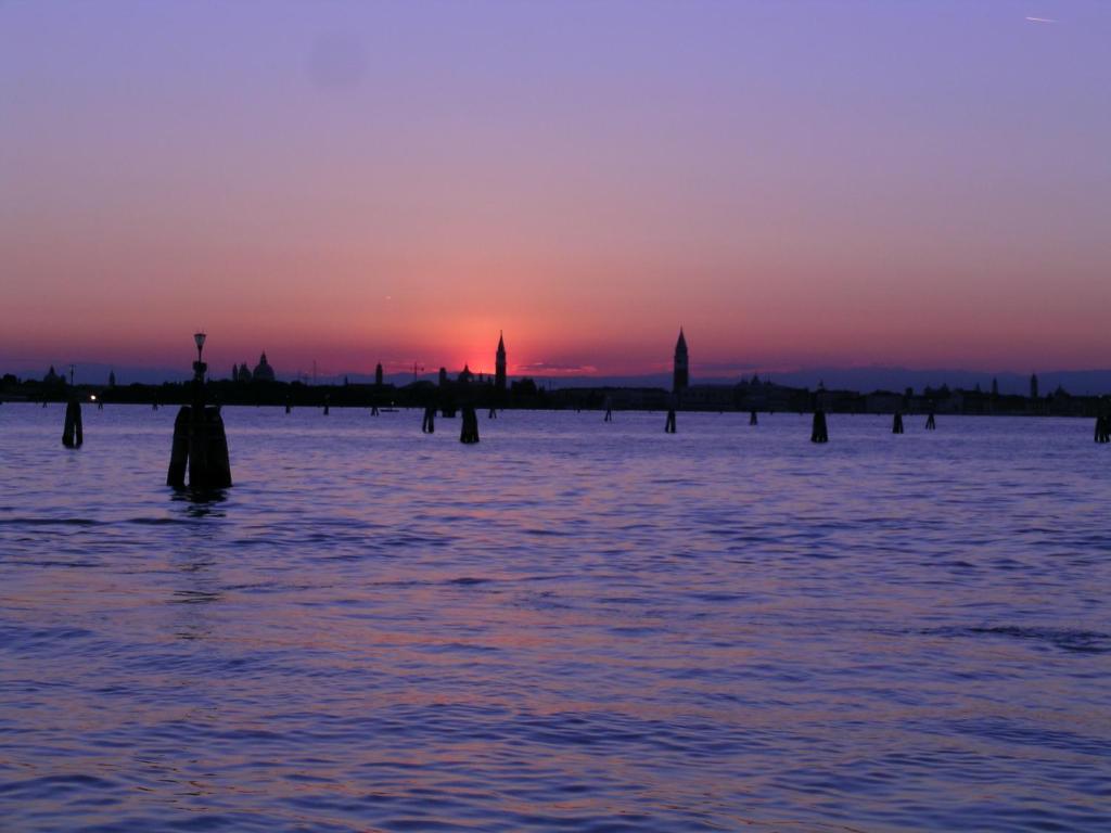 a sunset over the water with posts in the water at Hotel Belvedere in Venice-Lido