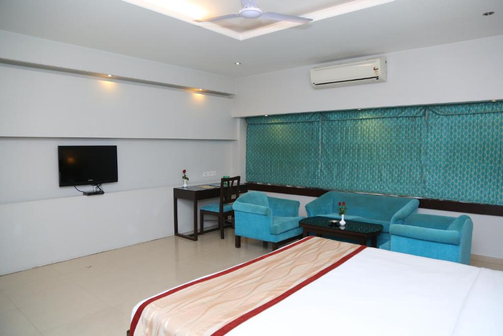 a room with a bed and chairs and a tv at The Curzon Court in Bangalore
