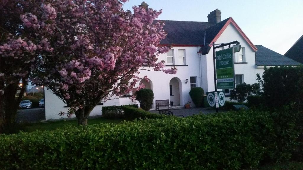 uma árvore com flores cor-de-rosa em frente a uma casa branca em The Old Cable Historic House & Seafood Restaurant em Waterville