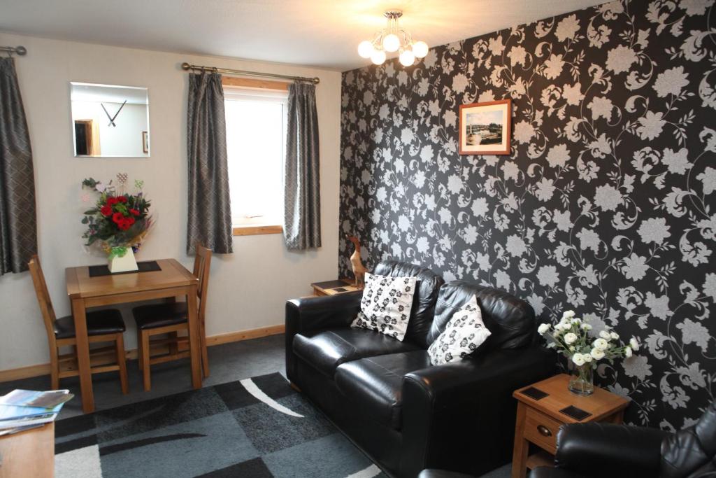 a living room with a black leather couch and floral wallpaper at Castleyards Apartment 1 in Kirkwall