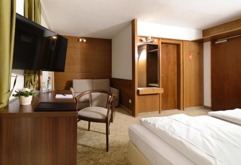 ein Hotelzimmer mit einem Bett und einem Schreibtisch mit Fernseher in der Unterkunft Hotel Bayerisch Meran in Bad Feilnbach