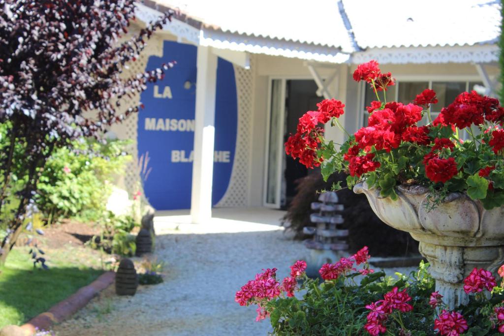 un vaso pieno di fiori rossi di fronte a un edificio di Maison Blanche a Lanton