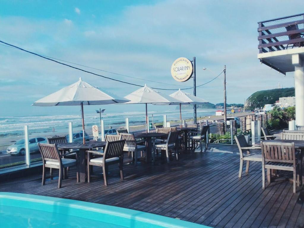 eine Terrasse mit Tischen und Stühlen und Blick auf den Strand in der Unterkunft Pousada Solar Inn in Torres